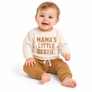 Baby in cream printed sweatshirt and brown joggers on pure white